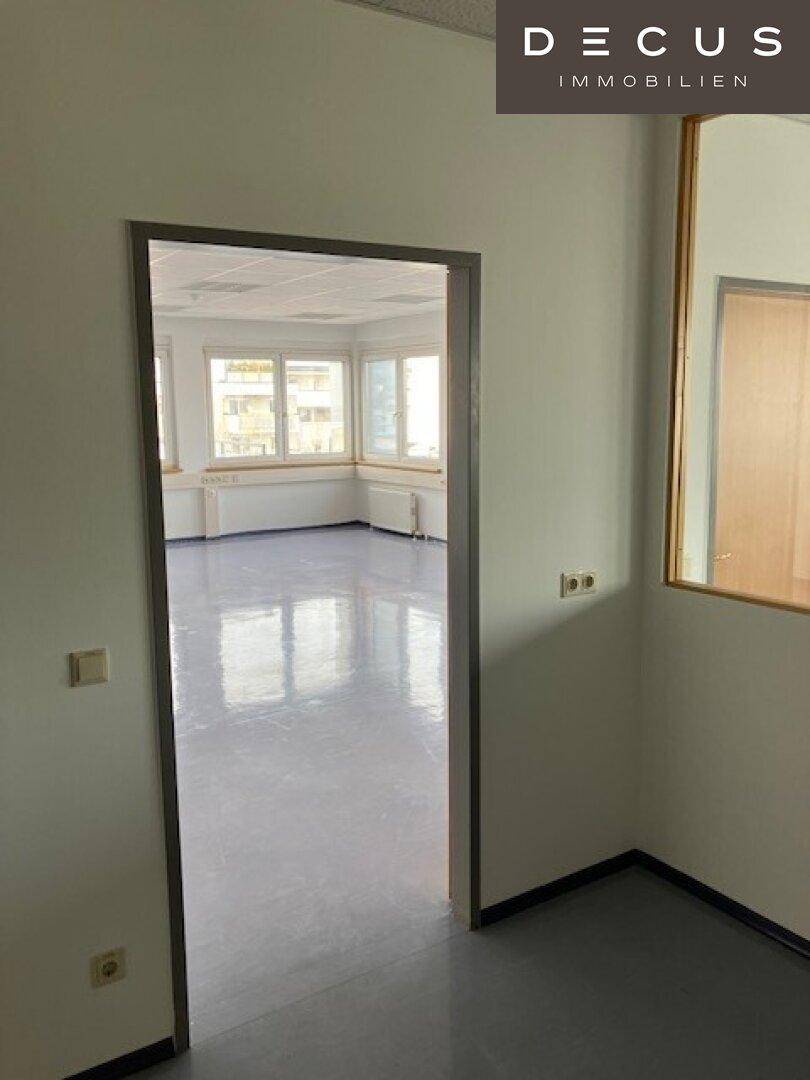Blick durch eine offene Tür in ein leeres Büro mit glänzendem Vinylboden und Fenstern.