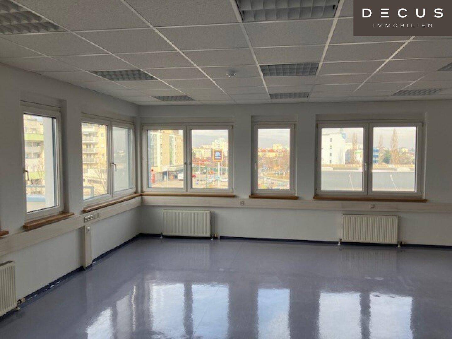 Großes, leeres Büro mit vielen Fenstern, hellgrauem Vinylboden und Heizkörpern.
