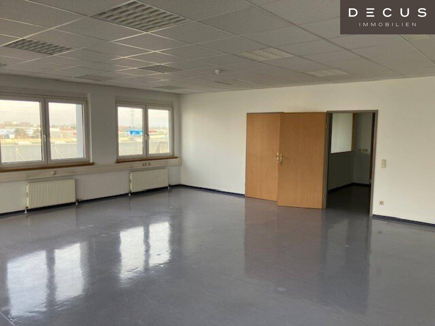 Großes, leeres Büro mit vielen Fenstern, hellgrauem Vinylboden und Doppeltüren.