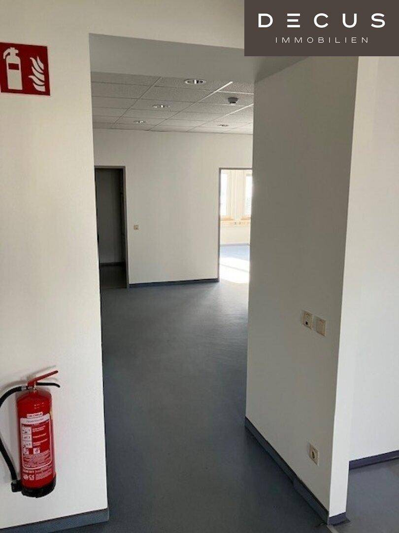 Heller Flur mit Vinylboden und Brandschutzvorrichtungen, der zu weiteren Büroräumen führt.