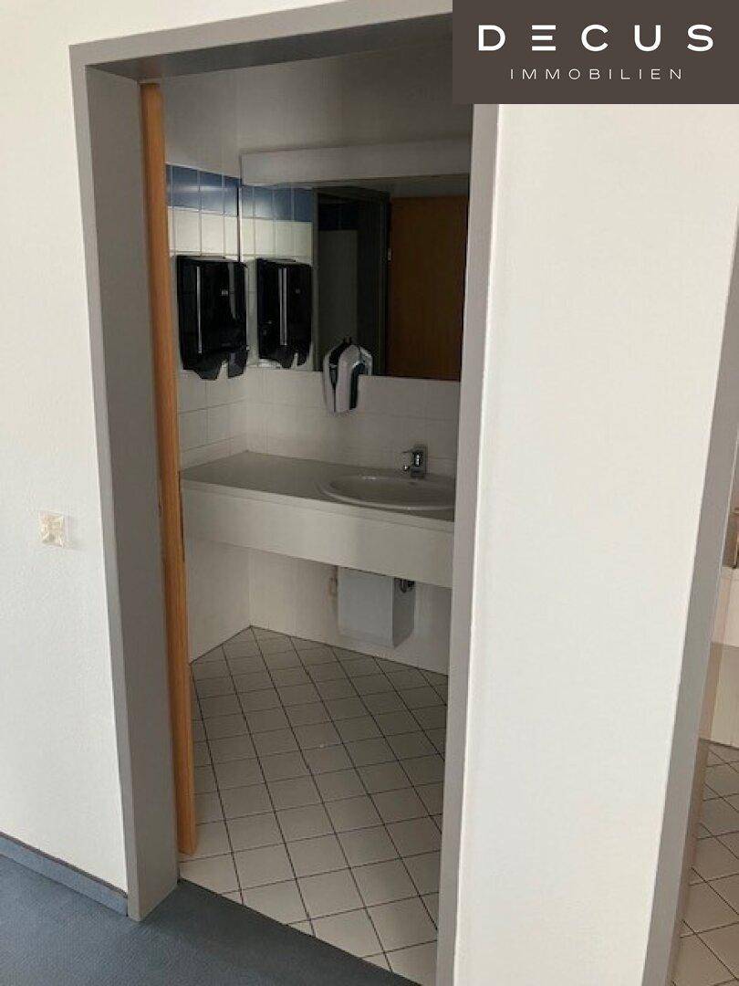 Waschraum mit Waschbecken, Spiegel und Fliesenboden, bereit für die Nutzung in einem Bürogebäude.