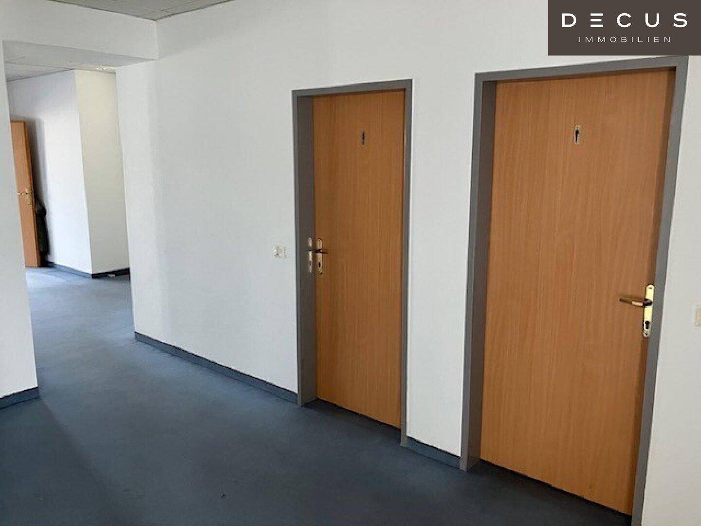 Heller Flur mit zwei Holztüren, die zu separaten Räumen führen, und Vinylboden.