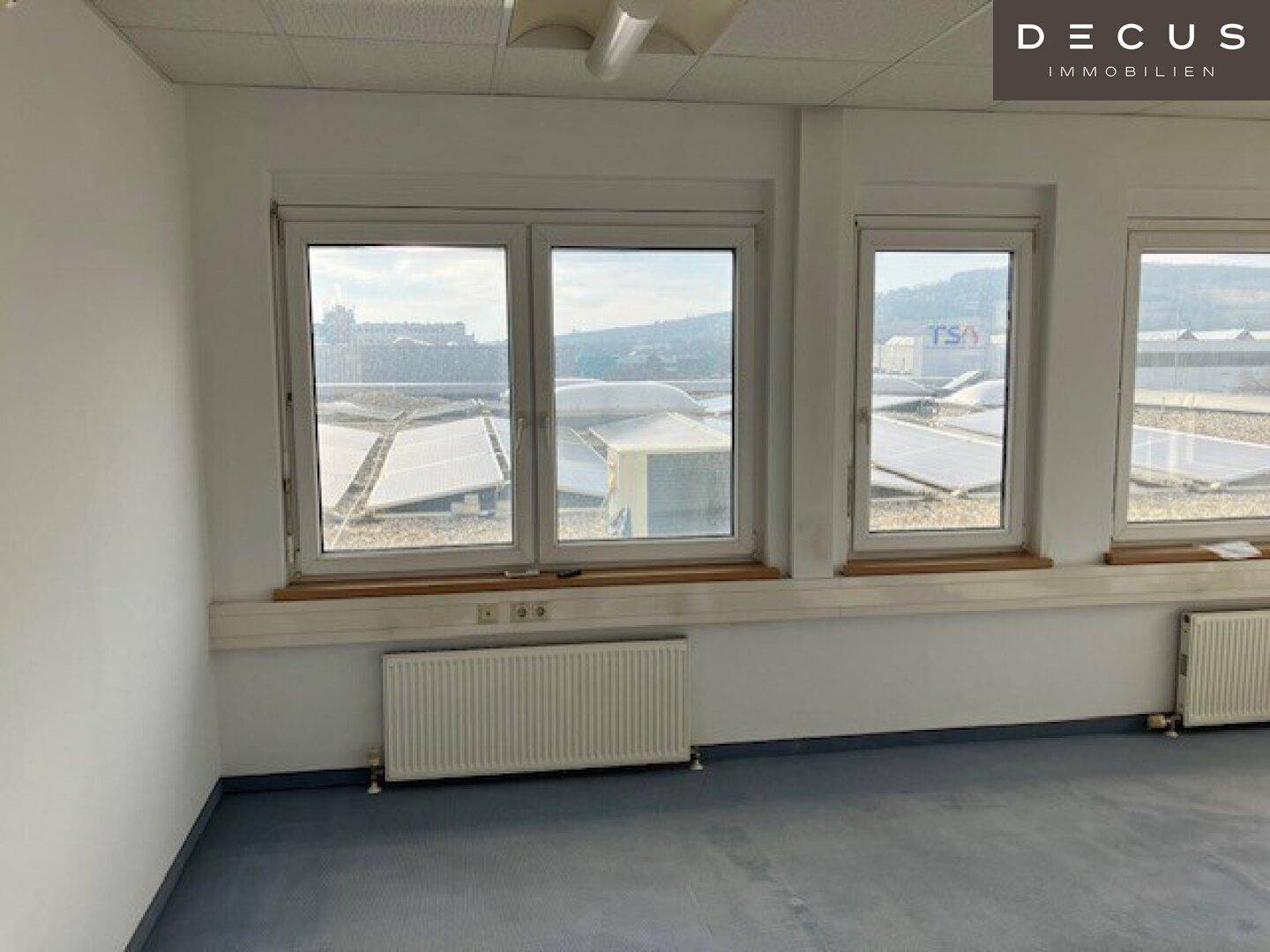 Büroraum mit großen Fenstern und Blick auf die Dächer mit Solaranlagen, viel Tageslicht.