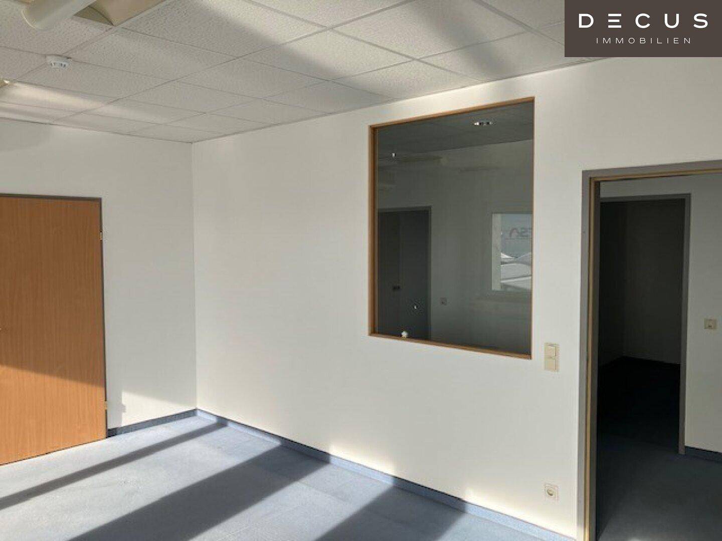 Büroraum mit Glaswand und Holztür, bietet eine helle und offene Arbeitsumgebung.