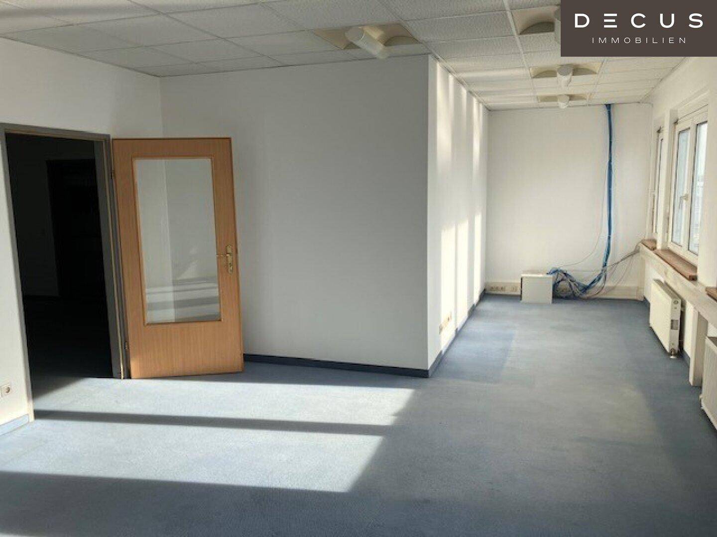 Heller Büroraum mit großen Fenstern und Kabelinstallationen, bereit für die Büronutzung.