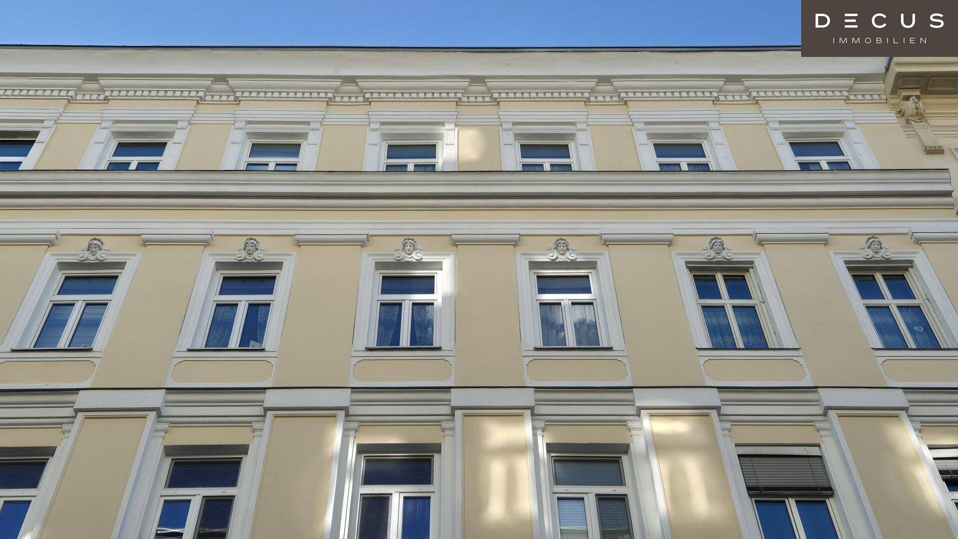 Nahaufnahme der oberen Fassade eines Gebäudes mit dekorativen Fensterrahmen und Gesimsen.
