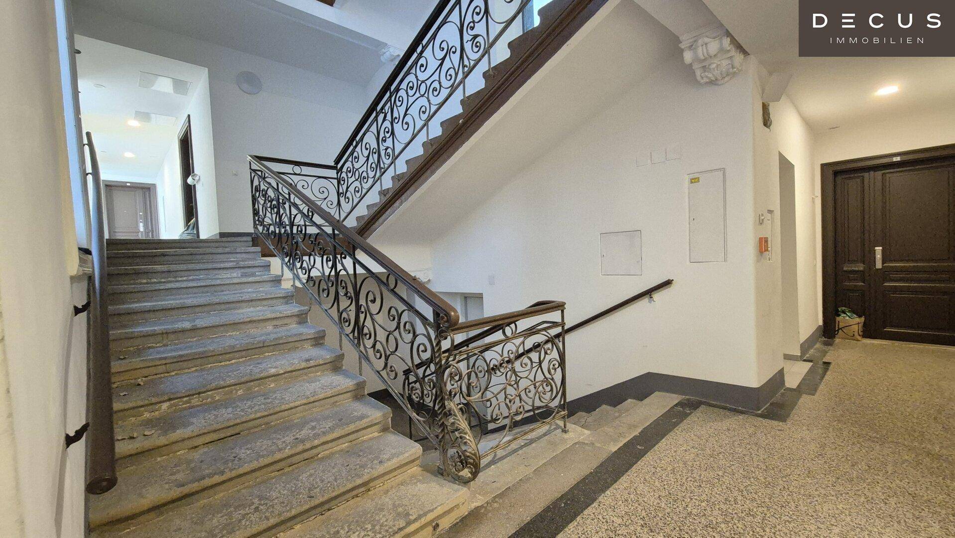 Historisches Treppenhaus mit schmiedeeisernem Geländer und Steinstufen in einem Altbau.