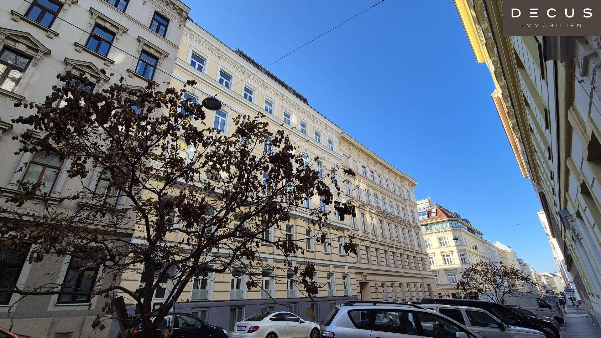 Historisches Gebäude mit vielen Fenstern und parkenden Autos an einer Stadtstraße.