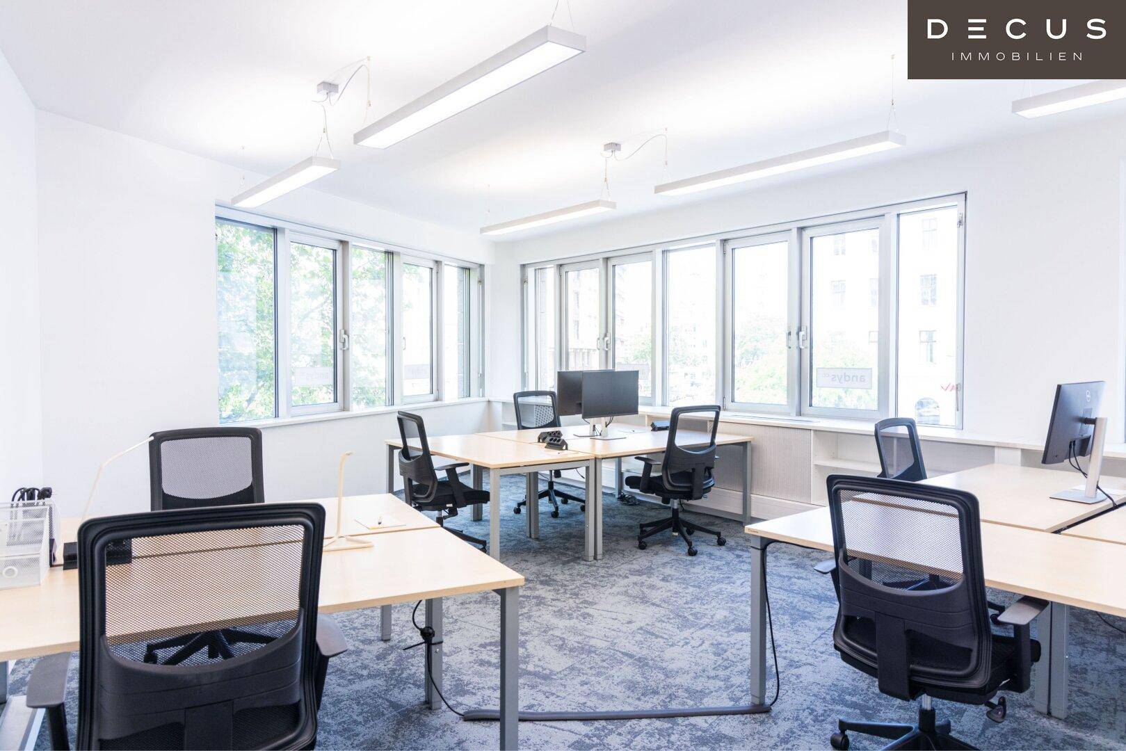 Helles Büro mit mehreren Arbeitsplätzen, großen Fenstern und einem angenehmen Blick ins Grüne.