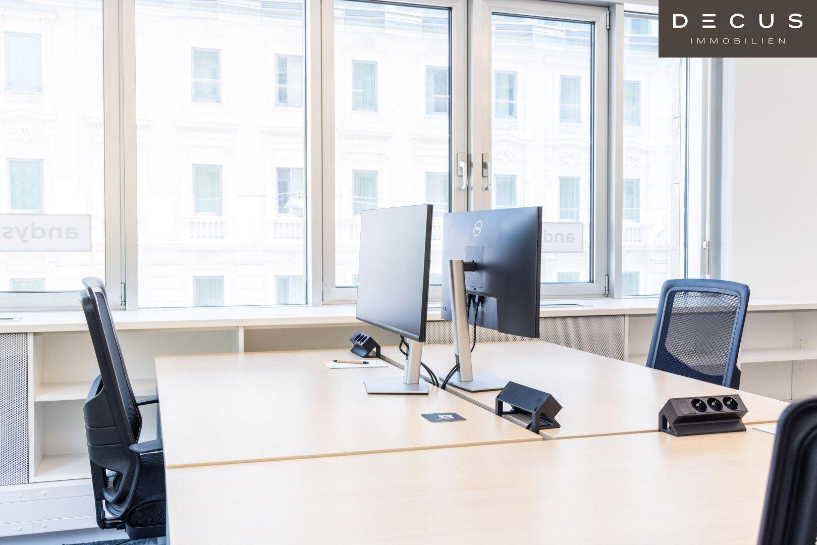 Detailansicht eines modernen Arbeitsplatzes mit Computermonitoren und weitem Blick aus dem Fenster.