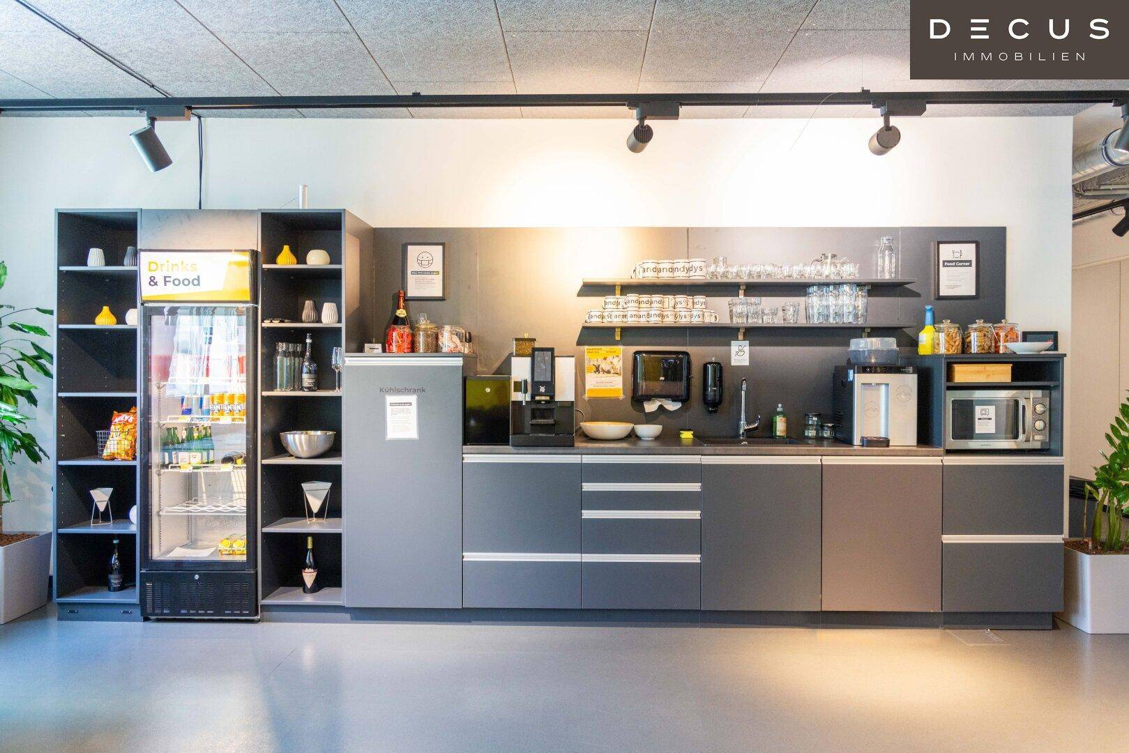 Moderne Küchenzeile in einem Bürobereich mit Kühlschrank, Mikrowelle und Kaffeemaschine.