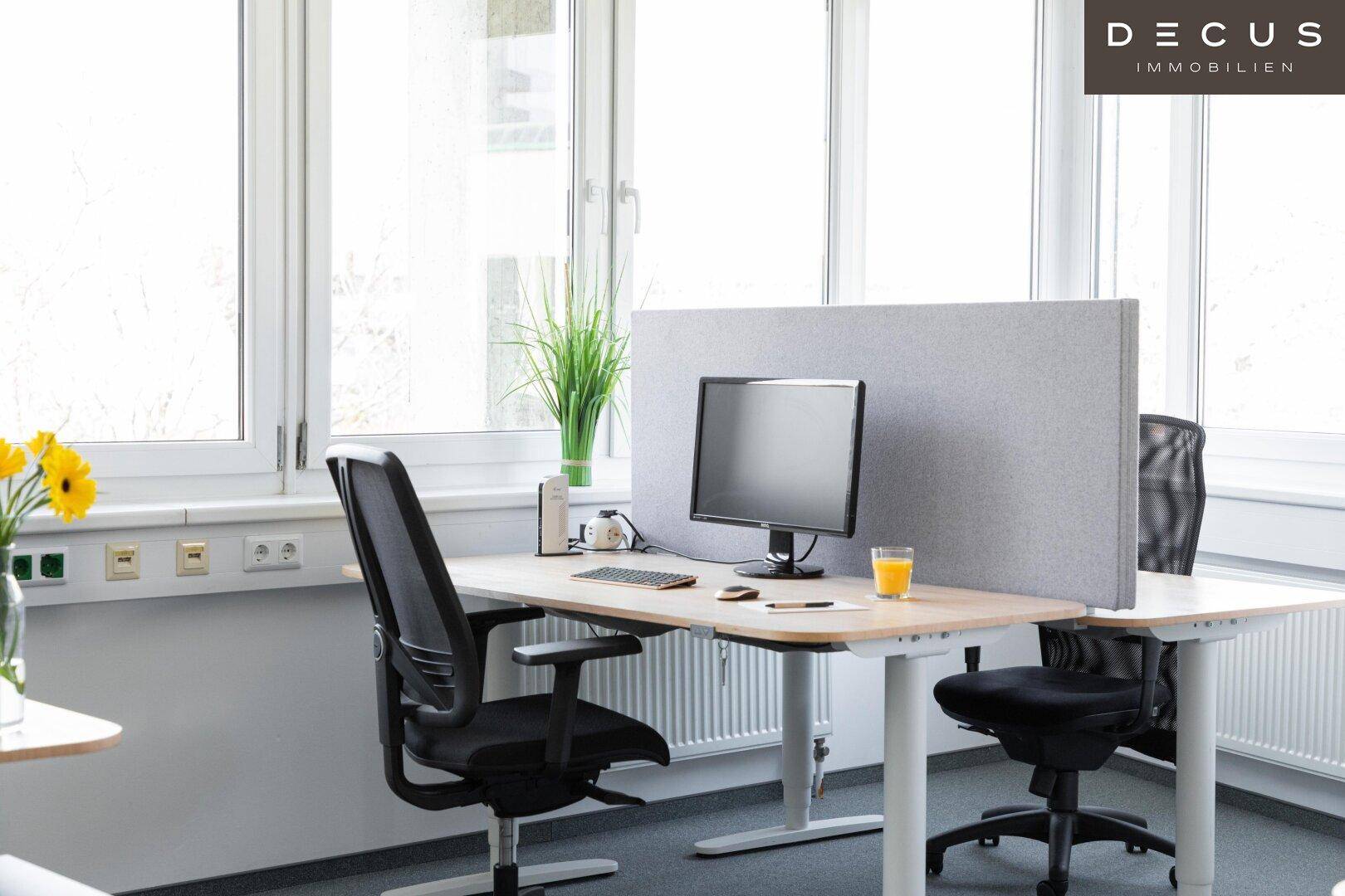 Heller Büroarbeitsplatz mit ergonomischem Stuhl, Monitor und großen Fenstern für natürliches Licht.