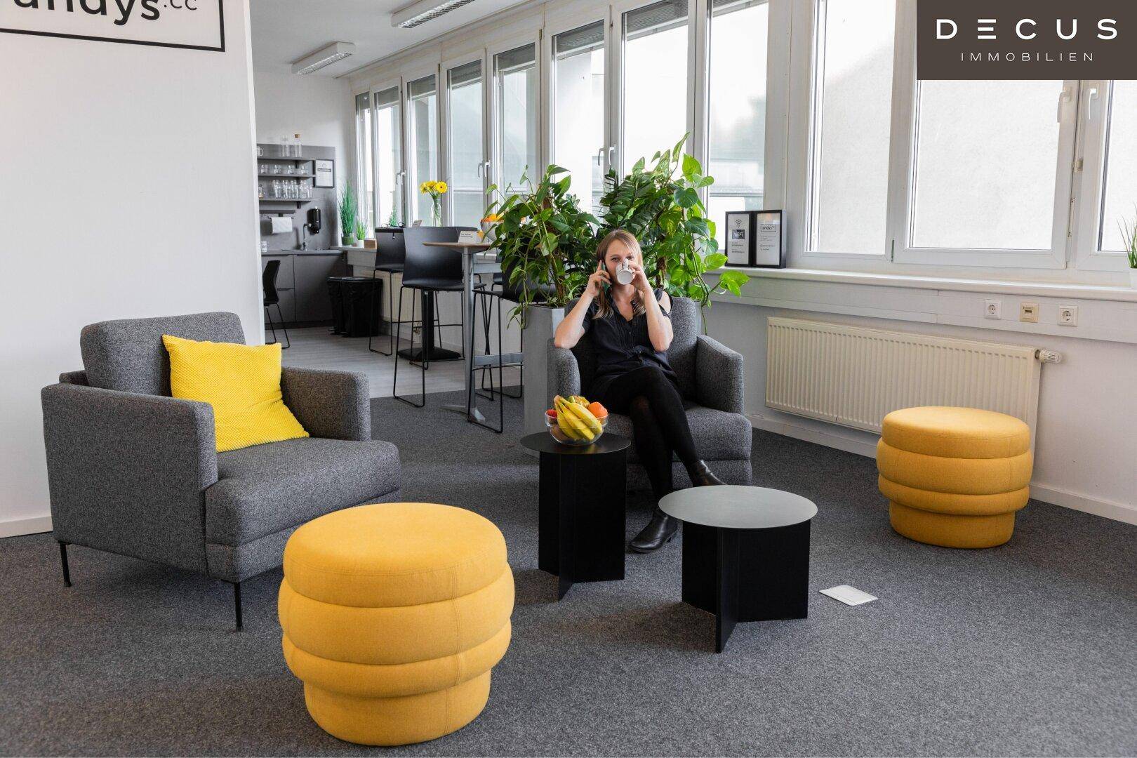 Gemütlicher Lounge-Bereich in einem Büro mit bequemen Sesseln, gelben Hockern und viel Grünpflanzen.