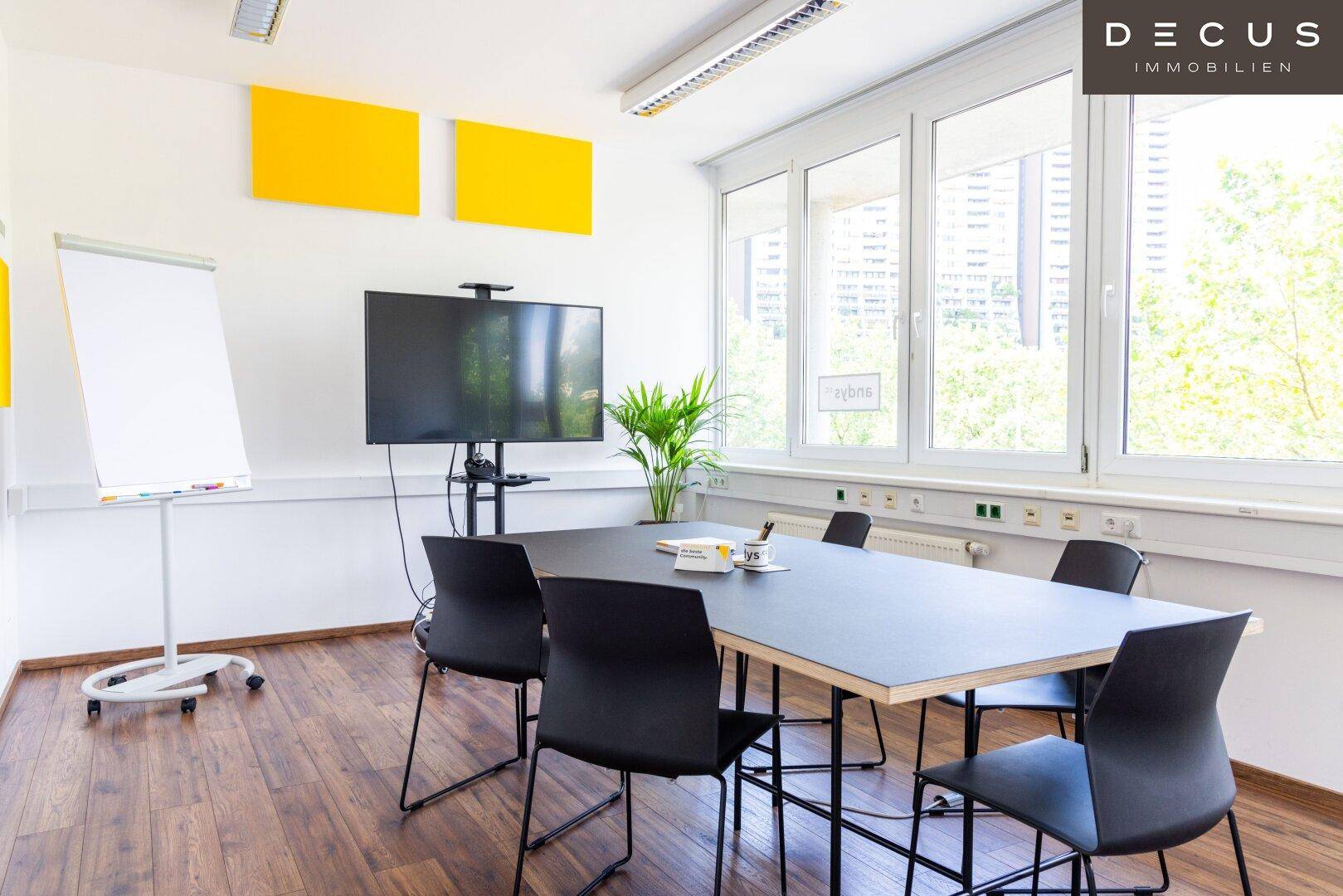 Moderner Konferenzraum mit großem Tisch, Präsentationsbildschirm und Holzboden, ideal für Besprechungen.