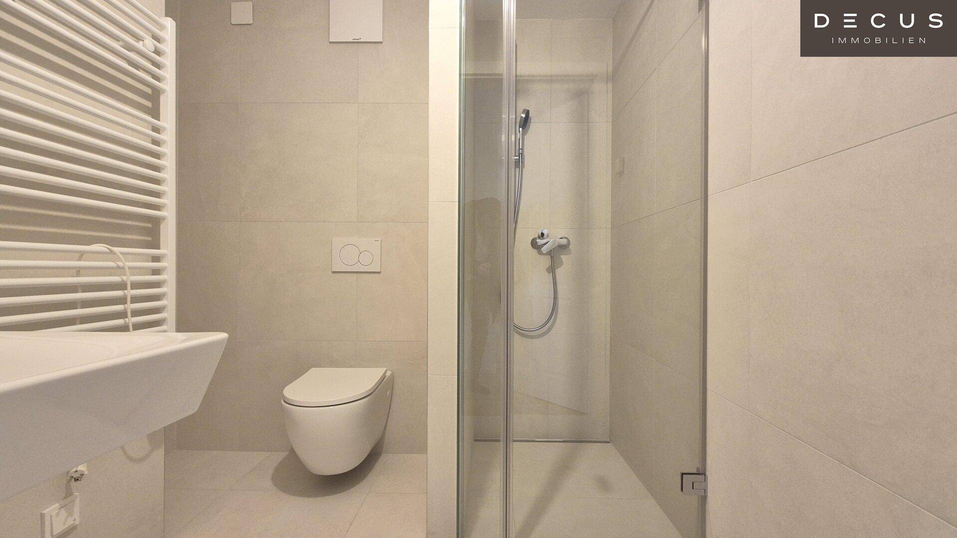 Modernes Badezimmer mit beigefarbenen Fliesen, wandhängendem WC und ebenerdiger Dusche.