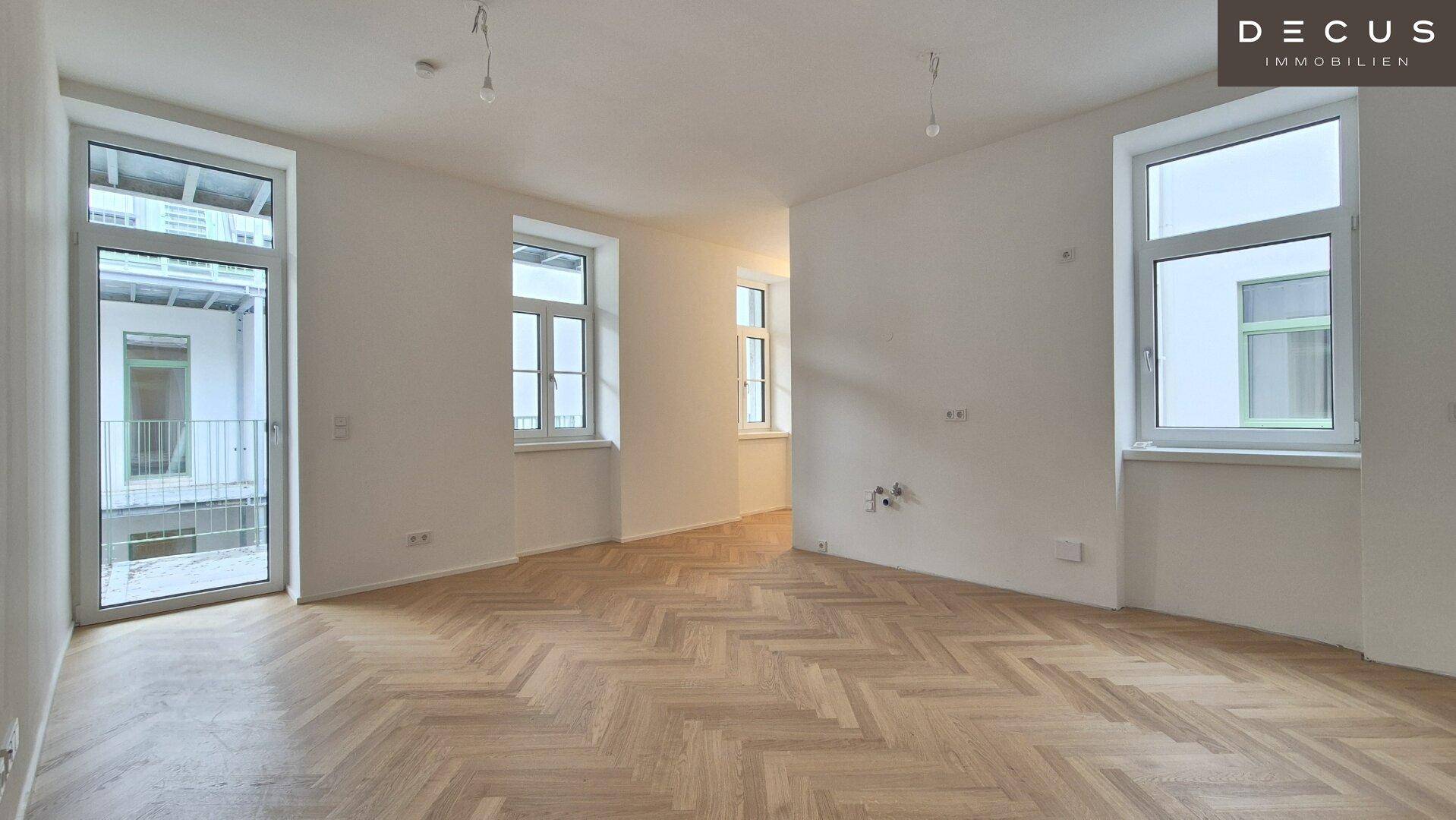 Geräumiges, helles Zimmer mit Fischgrätparkett und Zugang zu einem Balkon.