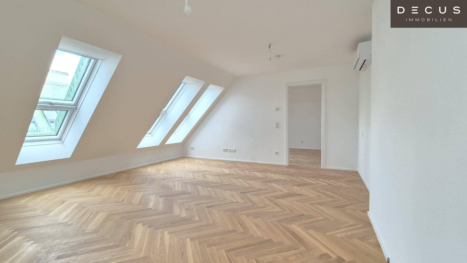 Helles Zimmer im Dachgeschoss mit schrägem Dach, Parkettboden und mehreren Dachfenstern.