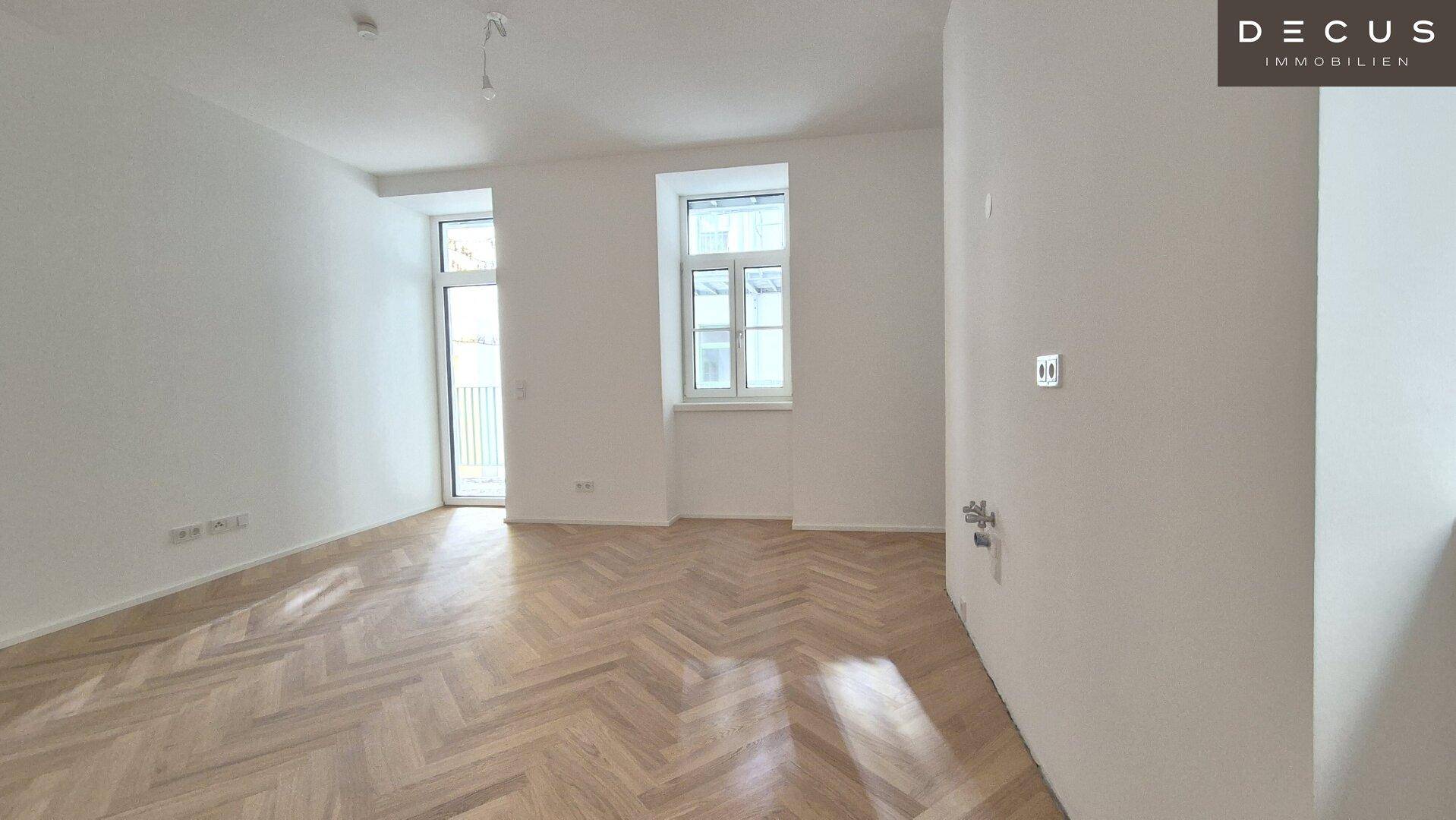 Geräumiges Zimmer mit Fischgrätparkett, hohen Decken und Zugang zu einem französischen Balkon.