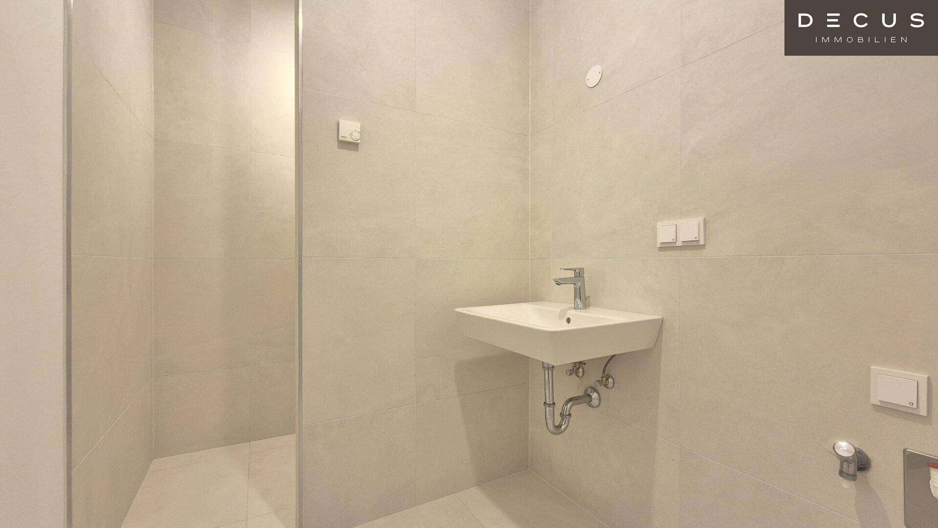 Modernes Badezimmer mit hellen Fliesen, wandhängendem Waschbecken und Duschbereich.