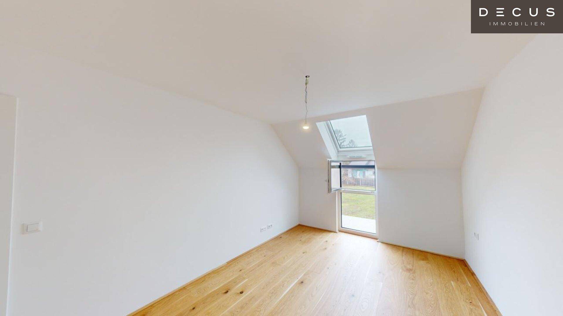 Geräumiges Dachgeschosszimmer mit Holzboden und schrägem Fenster, das viel Tageslicht bietet.