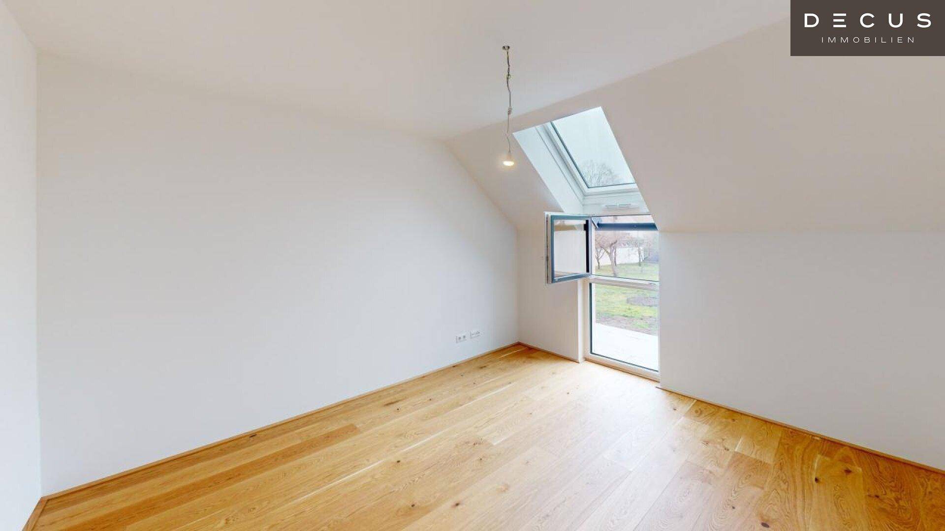 Schlafzimmer mit Holzboden und großem Dachfenster, das einen Blick ins Grüne bietet.