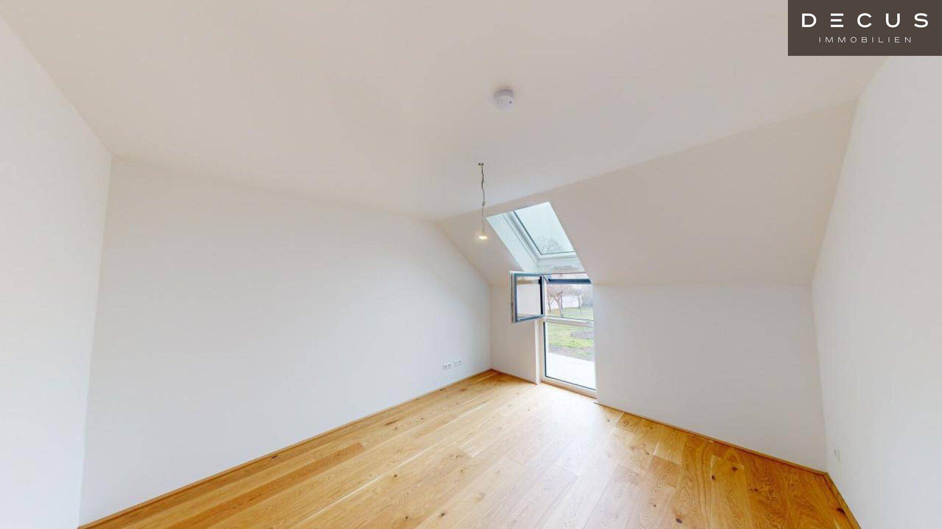 Helles Zimmer im Dachgeschoss mit Holzboden und großem Fenster, ideal als Schlafzimmer.