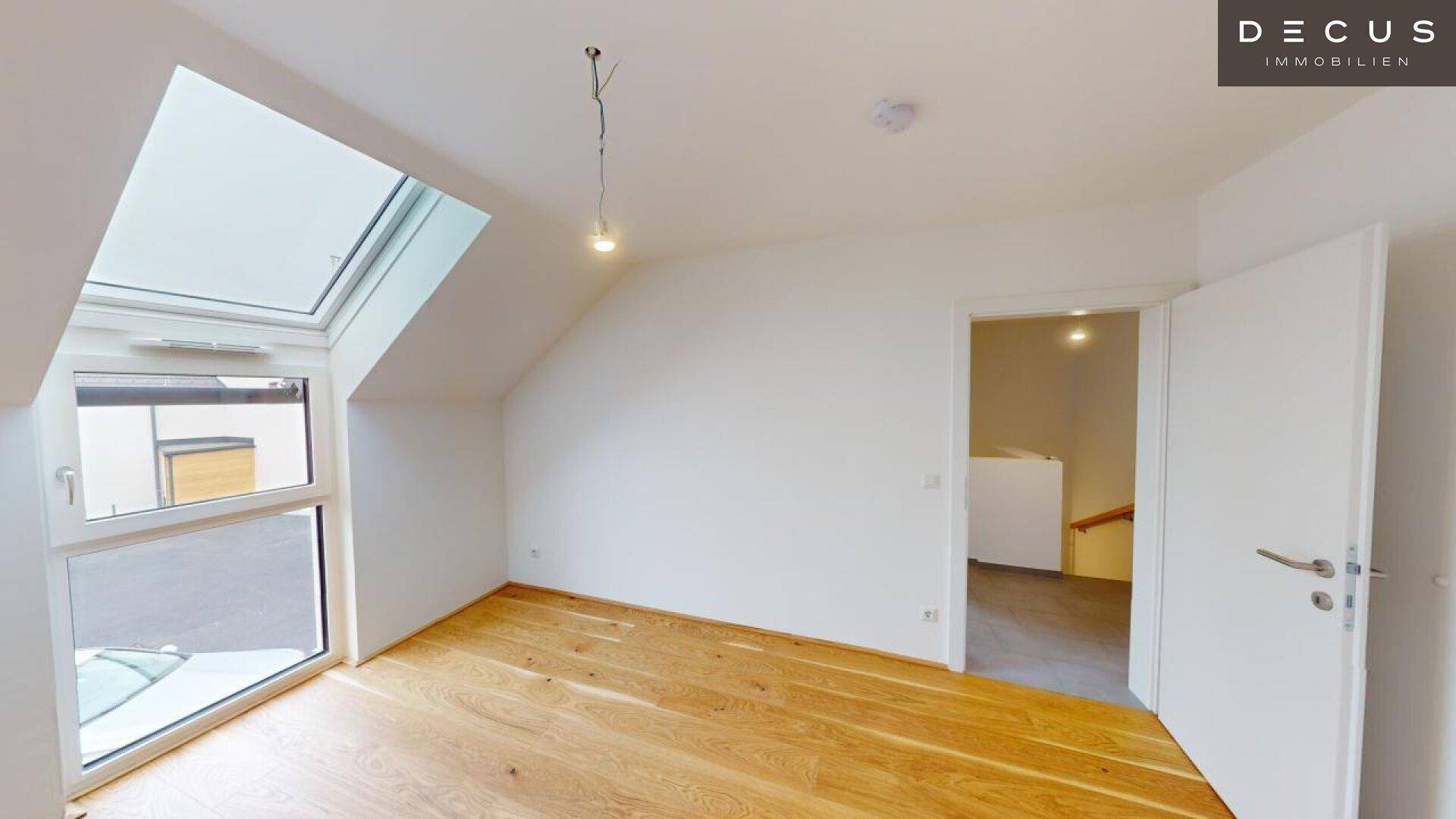 Dachgeschosszimmer mit Holzboden und schrägem Fenster, das viel Licht spendet.