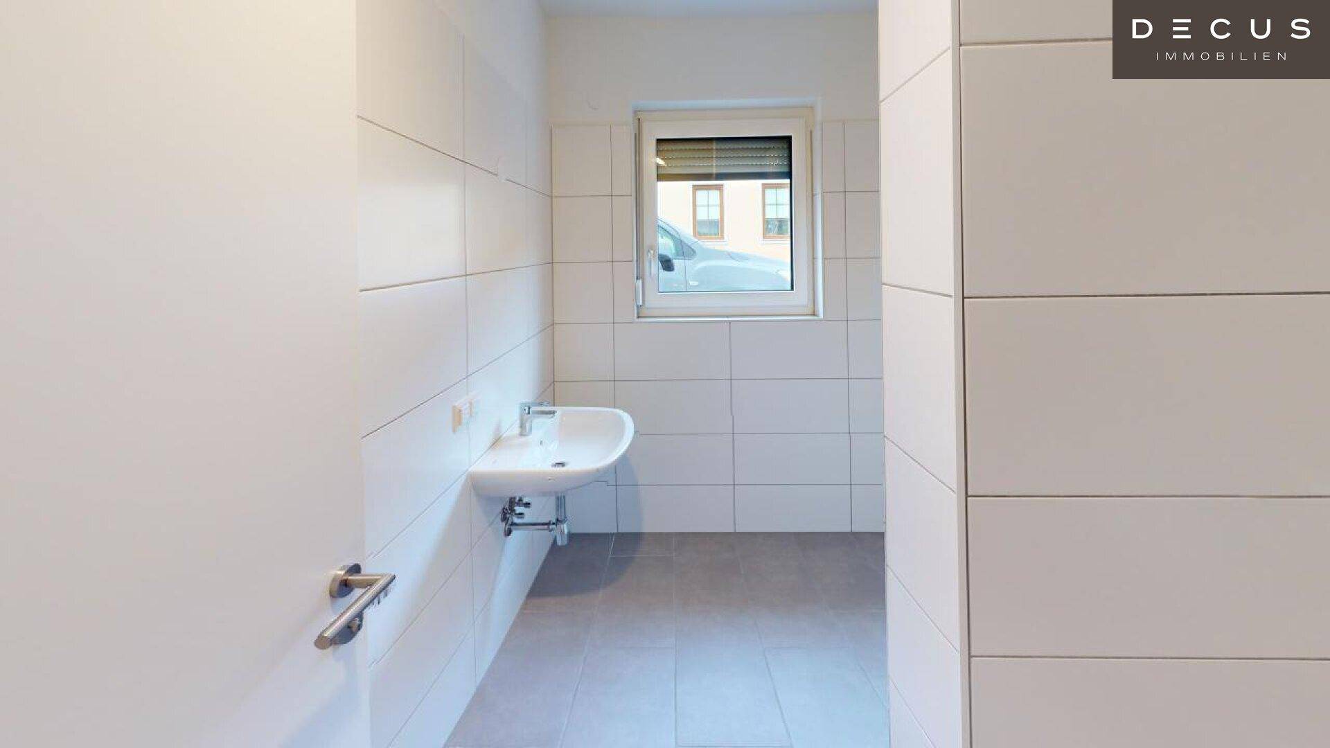 Modern gefliestes Badezimmer mit Waschbecken und Fenster, das viel Licht spendet.