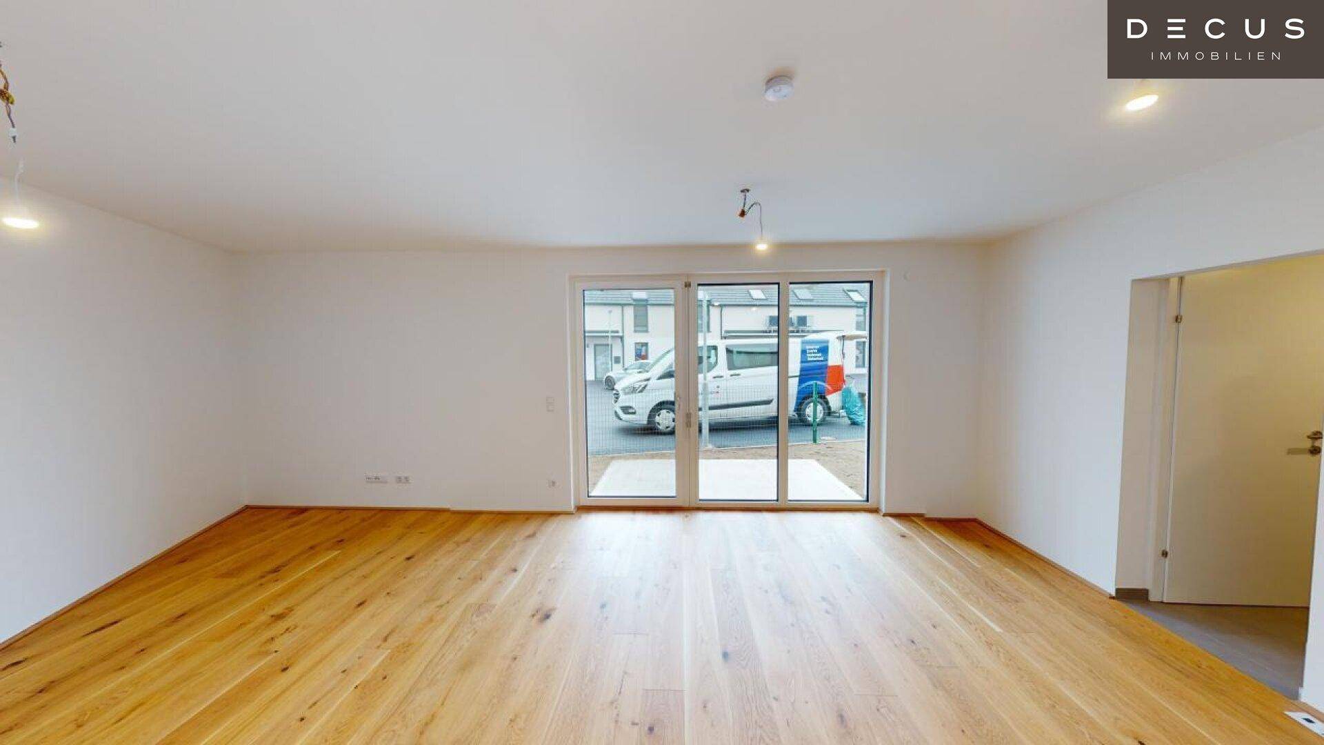 Heller Raum mit Holzboden und breiter Fensterfront, die den Blick nach draußen ermöglicht.