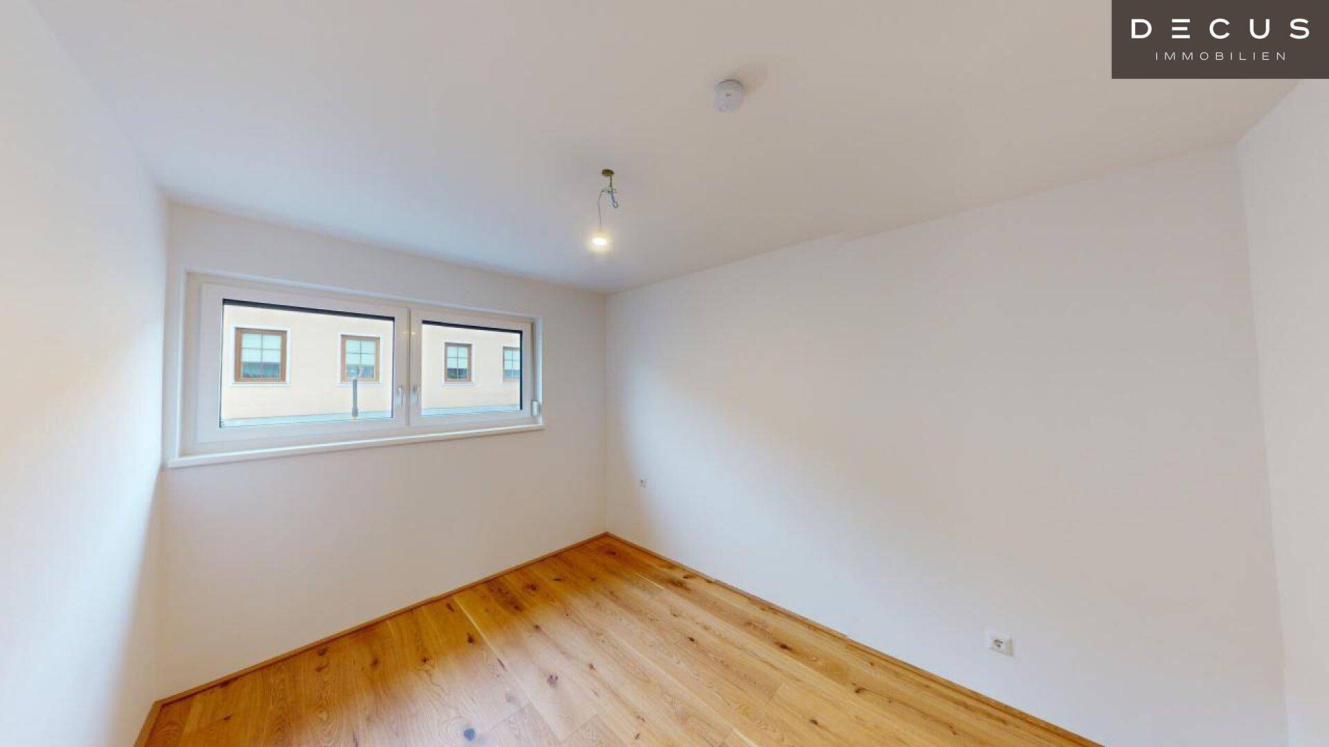 Helles Zimmer mit Holzboden und einem großen Fenster, ideal als Schlaf- oder Arbeitszimmer.