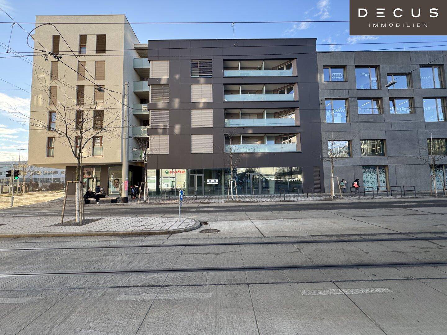 Gesamtansicht des modernen Gebäudekomplexes mit Geschäftsflächen und Wohnungen an einer belebten Straße.