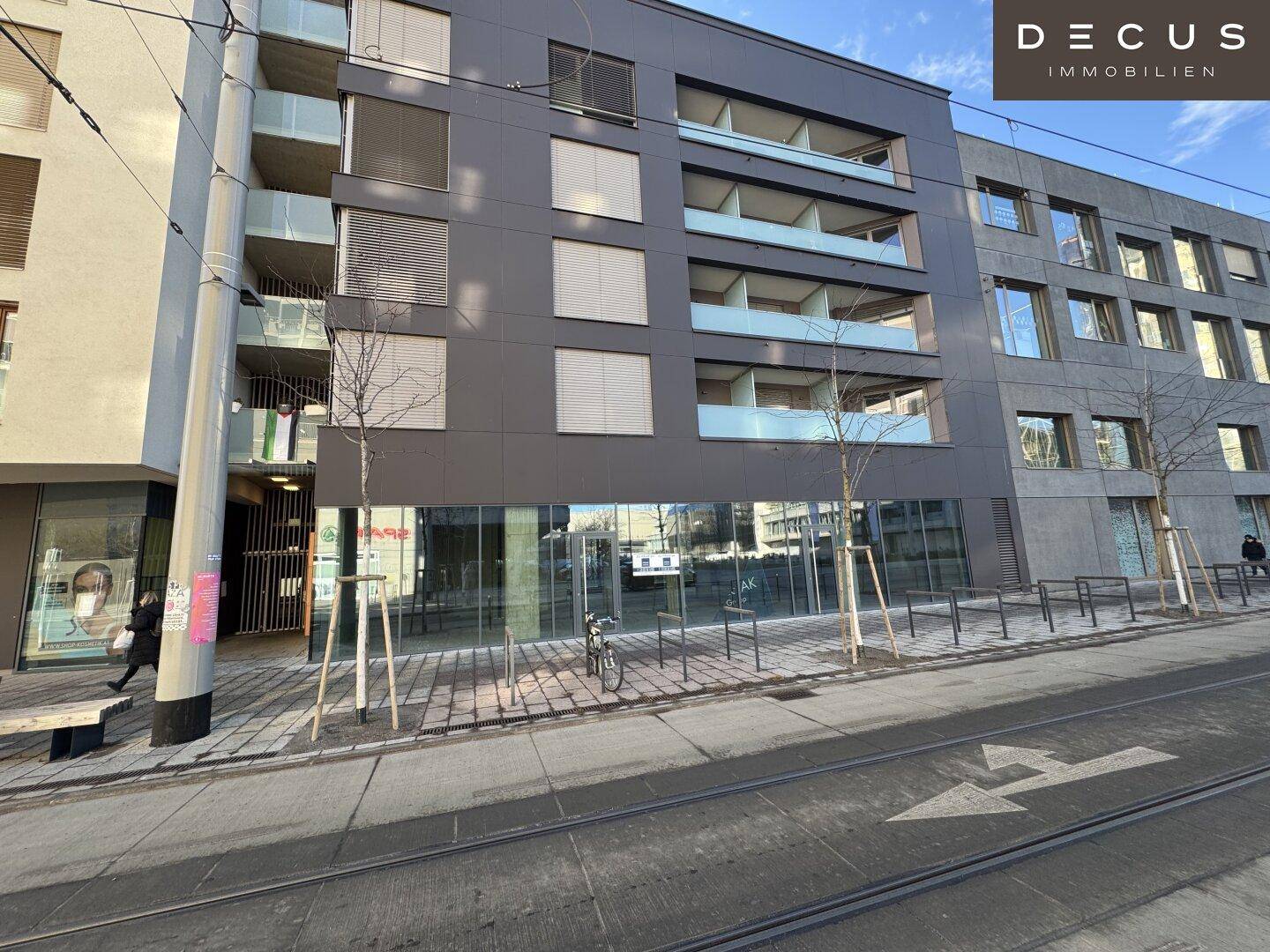 Blick auf die moderne Gebäudefassade mit Geschäftsräumen im Erdgeschoss und Wohnungen darüber.