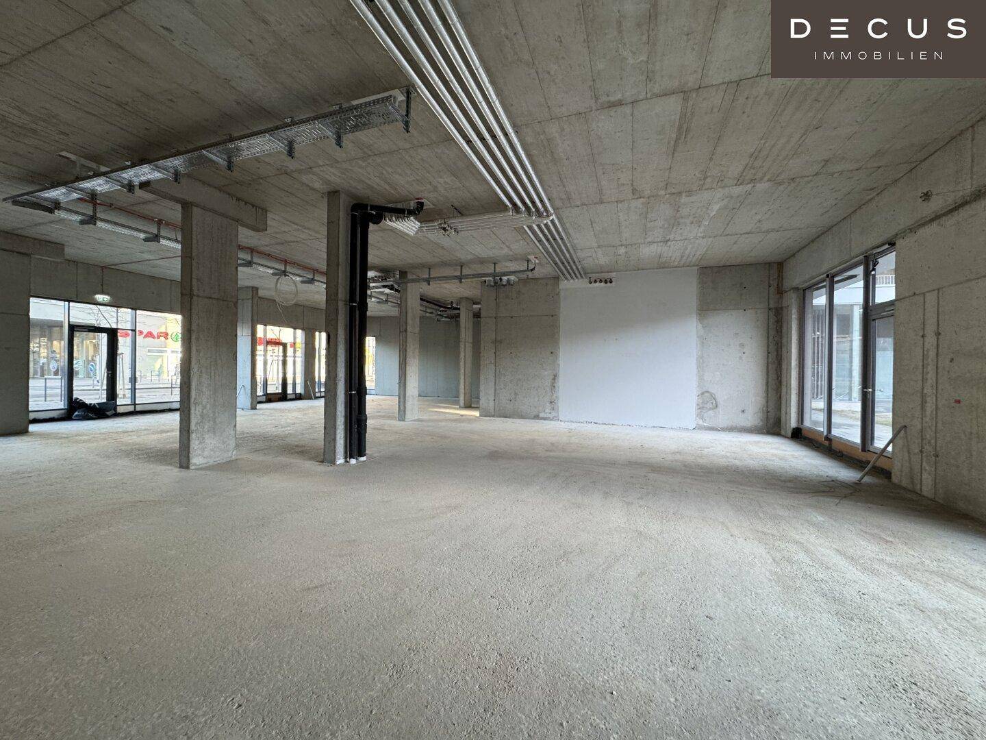 Weitläufiger, offener Gewerberaum mit Sichtbetonwänden und -decken, bereit für den Ausbau.