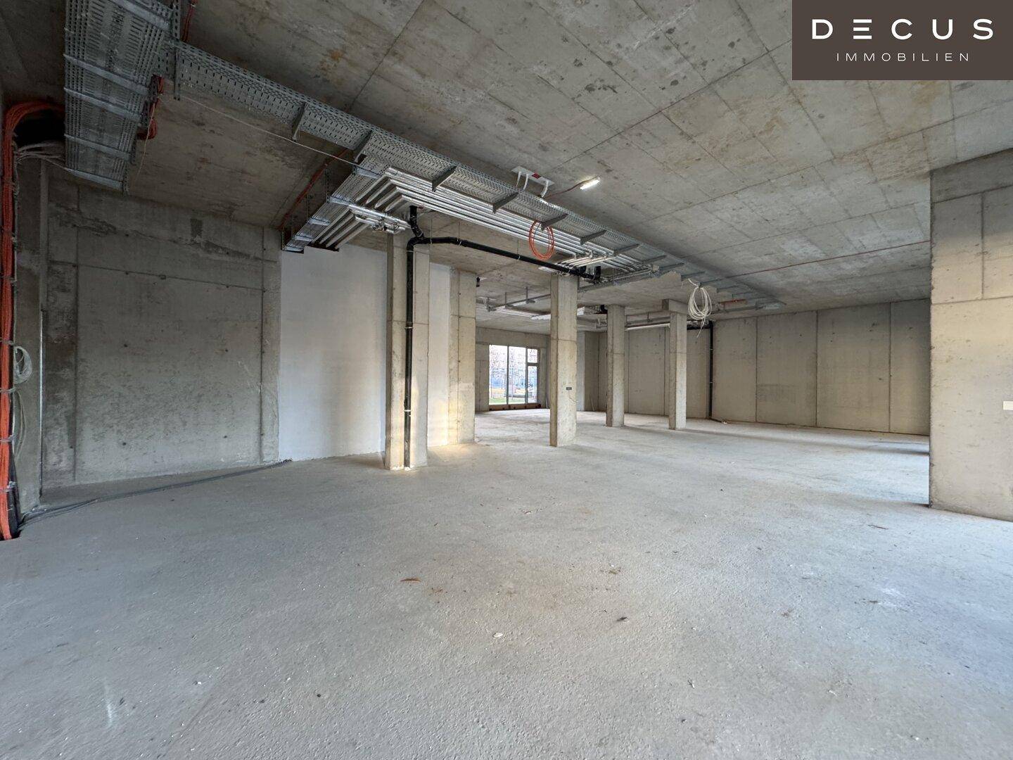 Großzügiger Gewerberaum im Rohbau mit Betonstützen und freiliegenden Deckeninstallationen.