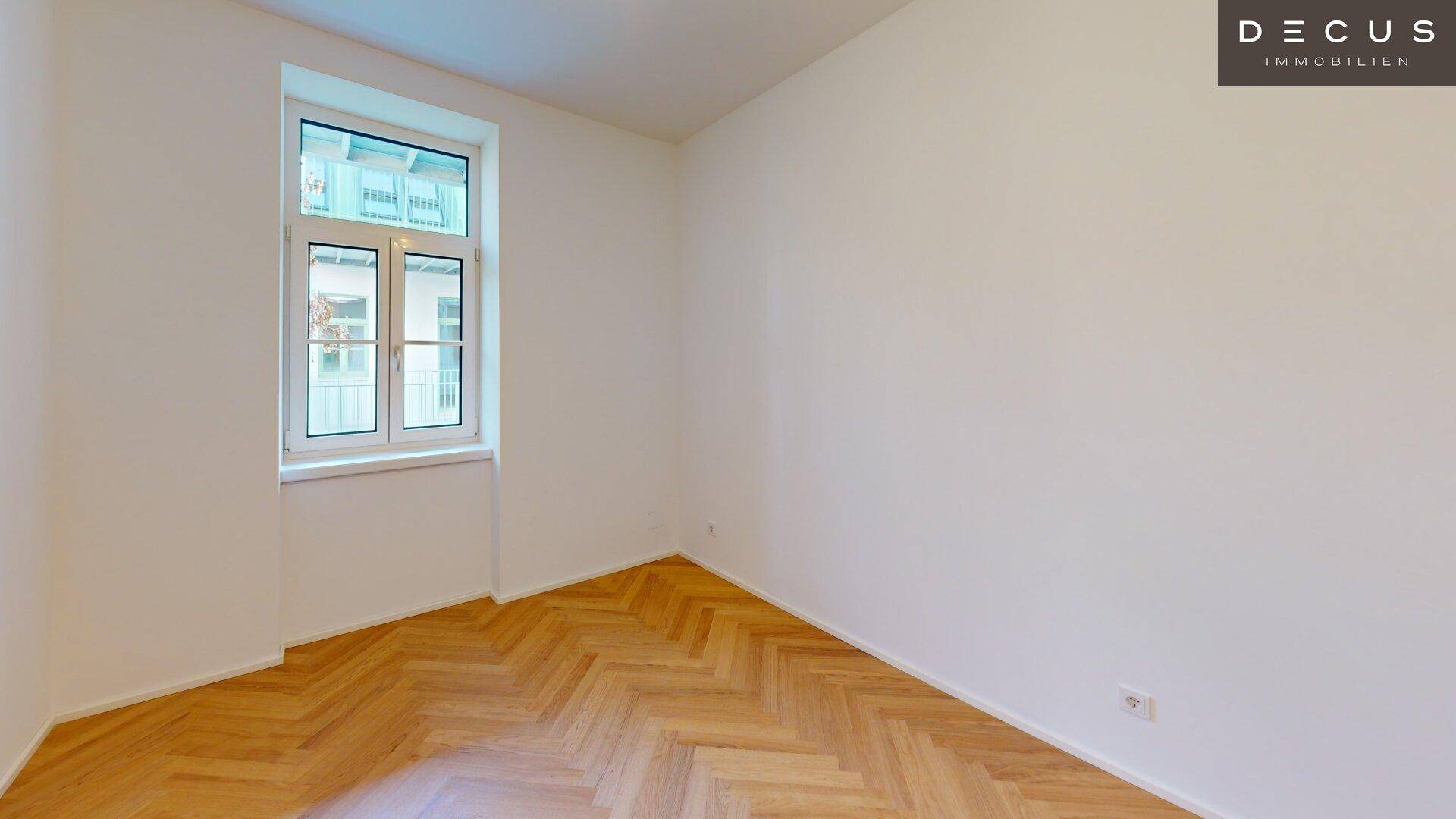 Helles Schlafzimmer mit Fischgrätparkettboden und einem Fenster mit Blick in den ruhigen Innenhof.