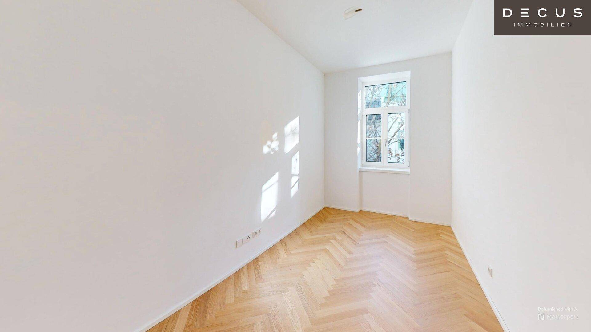 Lichtdurchfluteter Raum mit Fischgrätparkett und einem Fenster, das einen angenehmen Blick ins Grüne bietet.