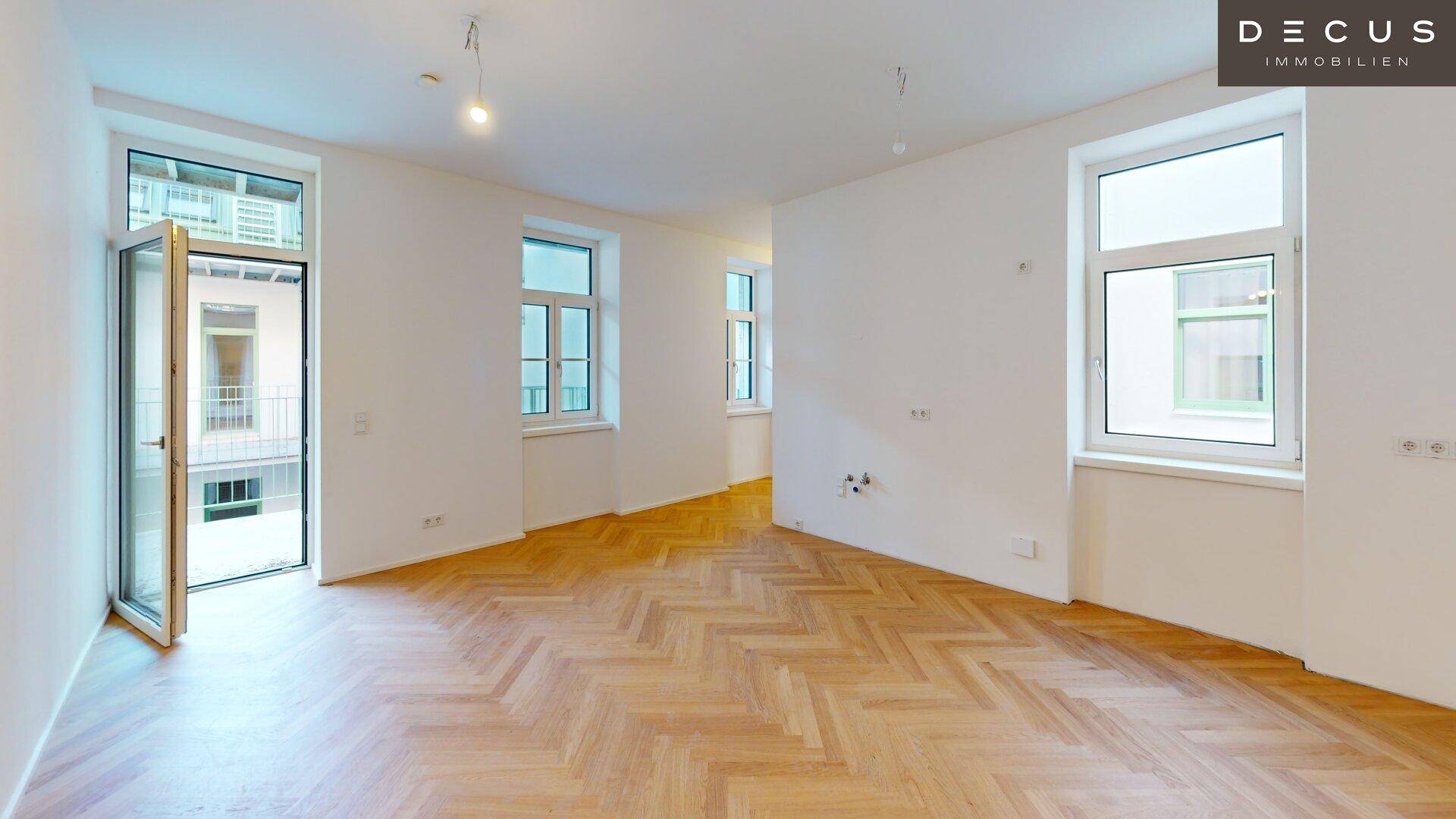 Heller Wohnraum mit Fischgrätparkettboden und Zugang zu einem Außenbereich mit Innenhofblick.