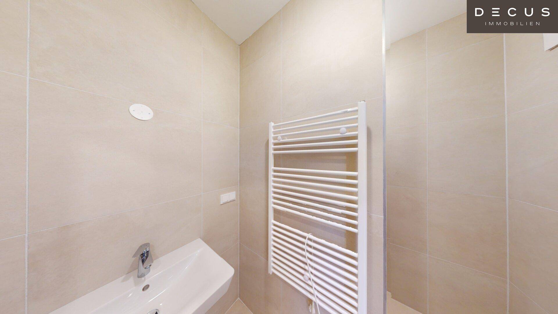 Modernes Badezimmer mit hellen Fliesen, einem Waschbecken und einem praktischen beheizten Handtuchhalter.