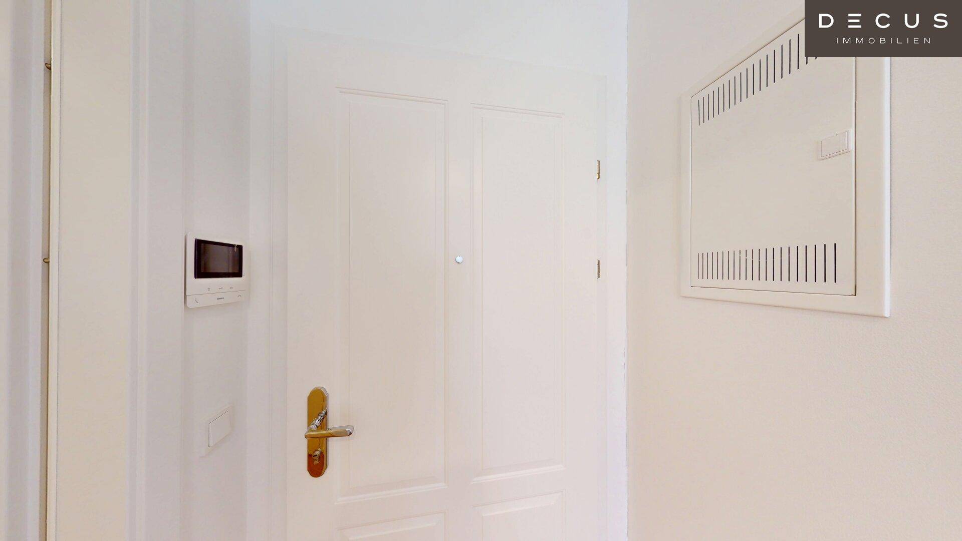 Eingangsbereich mit weißer Tür, Gegensprechanlage und einem Sicherungskasten an der Wand.