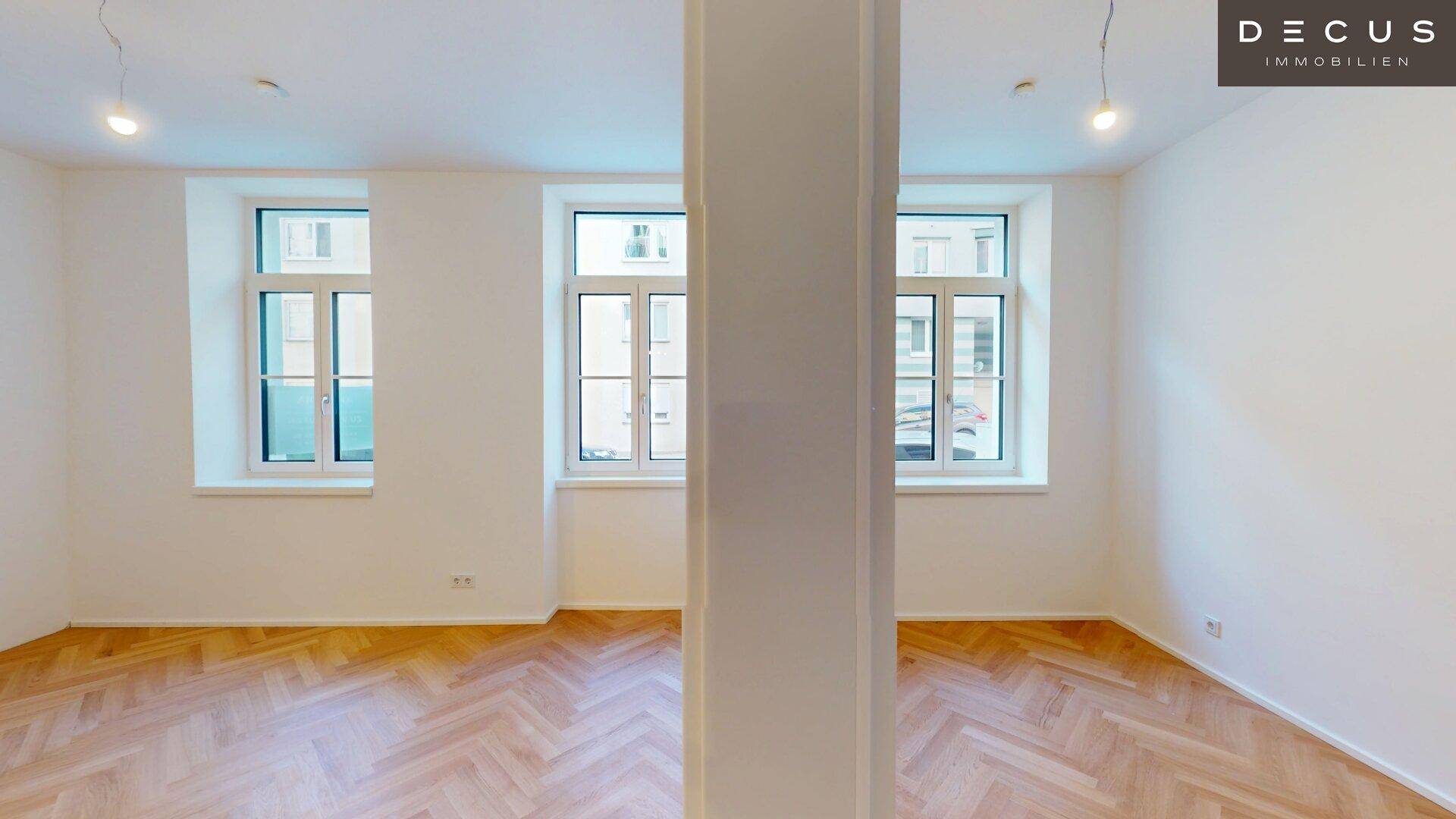 Helles Wohnzimmer mit Fischgrätparkett, hohen Decken und drei großen Fenstern.