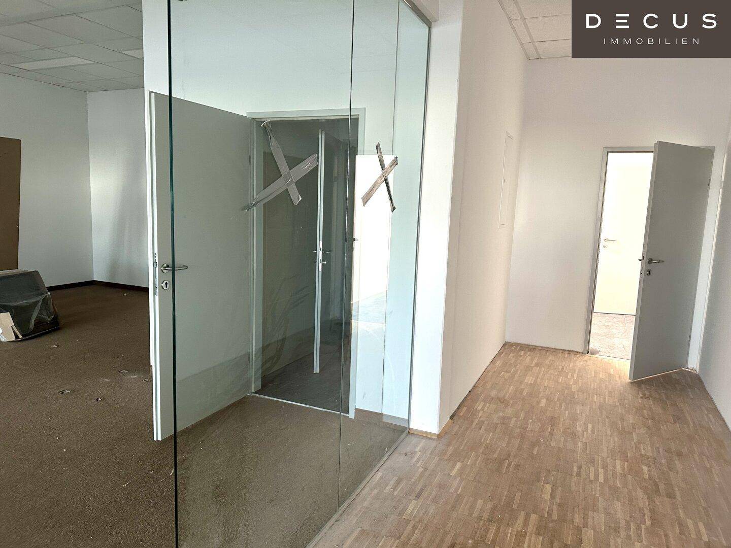 Flur mit Teppichboden und Parkett, der zu Büroräumen mit Glaswänden und Holztüren führt.