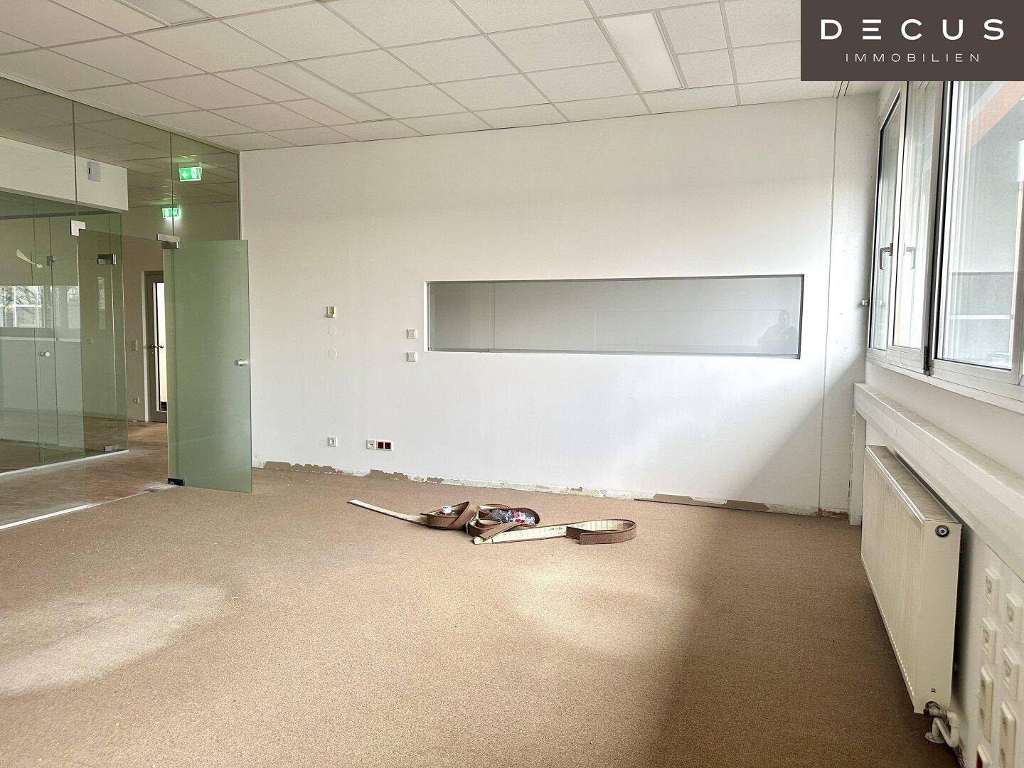 Bürofläche mit Teppichboden, großen Fenstern und einer schmalen Fensteröffnung zur Flurseite.