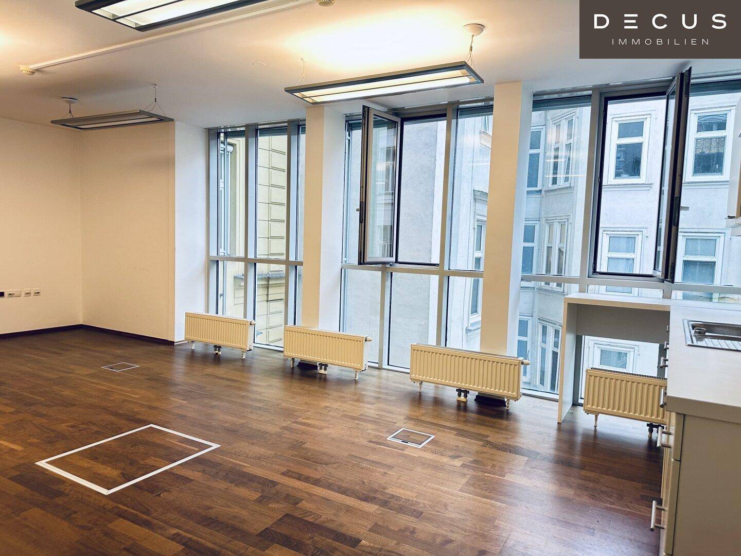 Heller Büroraum mit zahlreichen Fenstern, Holzboden und einer kleinen Arbeitsfläche, ideal für flexible Nutzung.