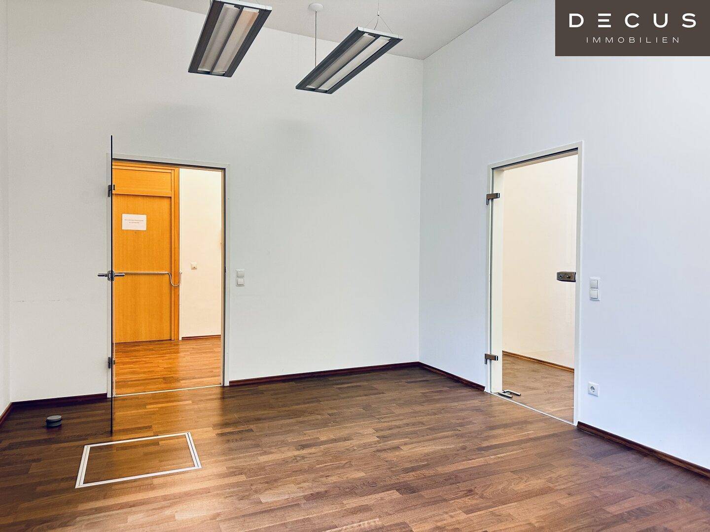 Leerer Büroraum mit Holzboden und zwei Türen, eine davon aus Glas, bietet flexible Raumgestaltung.