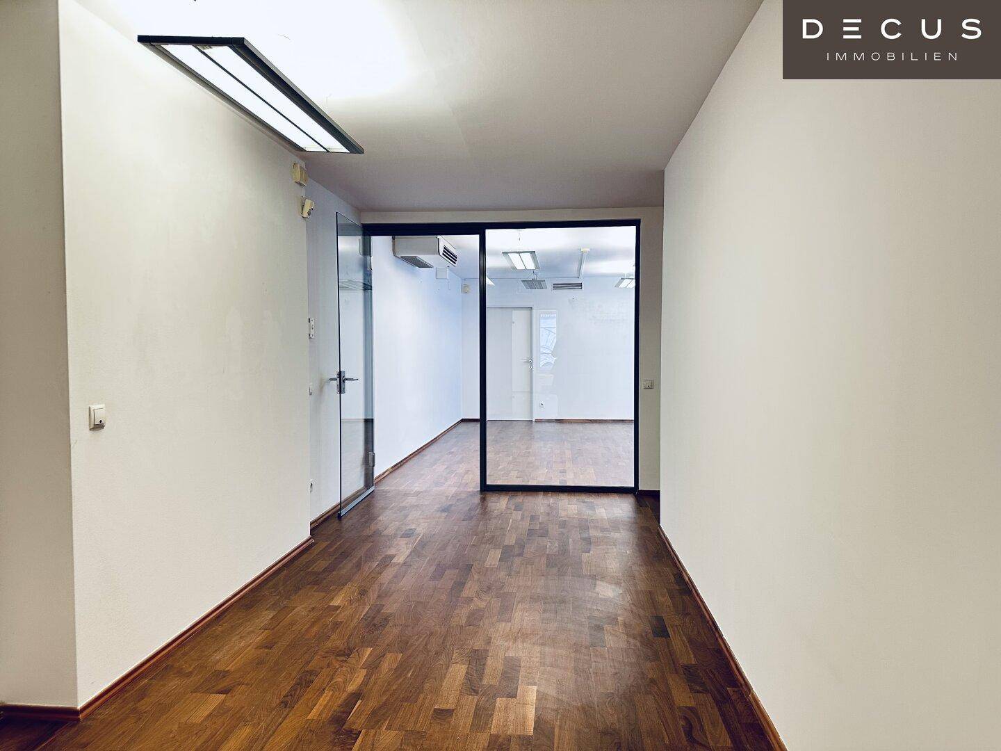 Moderner Flur mit Holzboden und eleganten Glaswänden, der eine offene und lichtdurchflutete Verbindung zwischen den Räumen schafft.