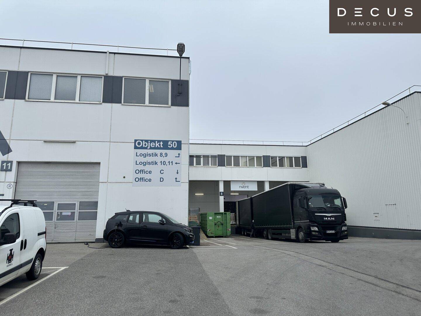 Außenansicht eines Gewerbegebäudes mit Laderampen und Parkplätzen für LKWs und Lieferwagen.