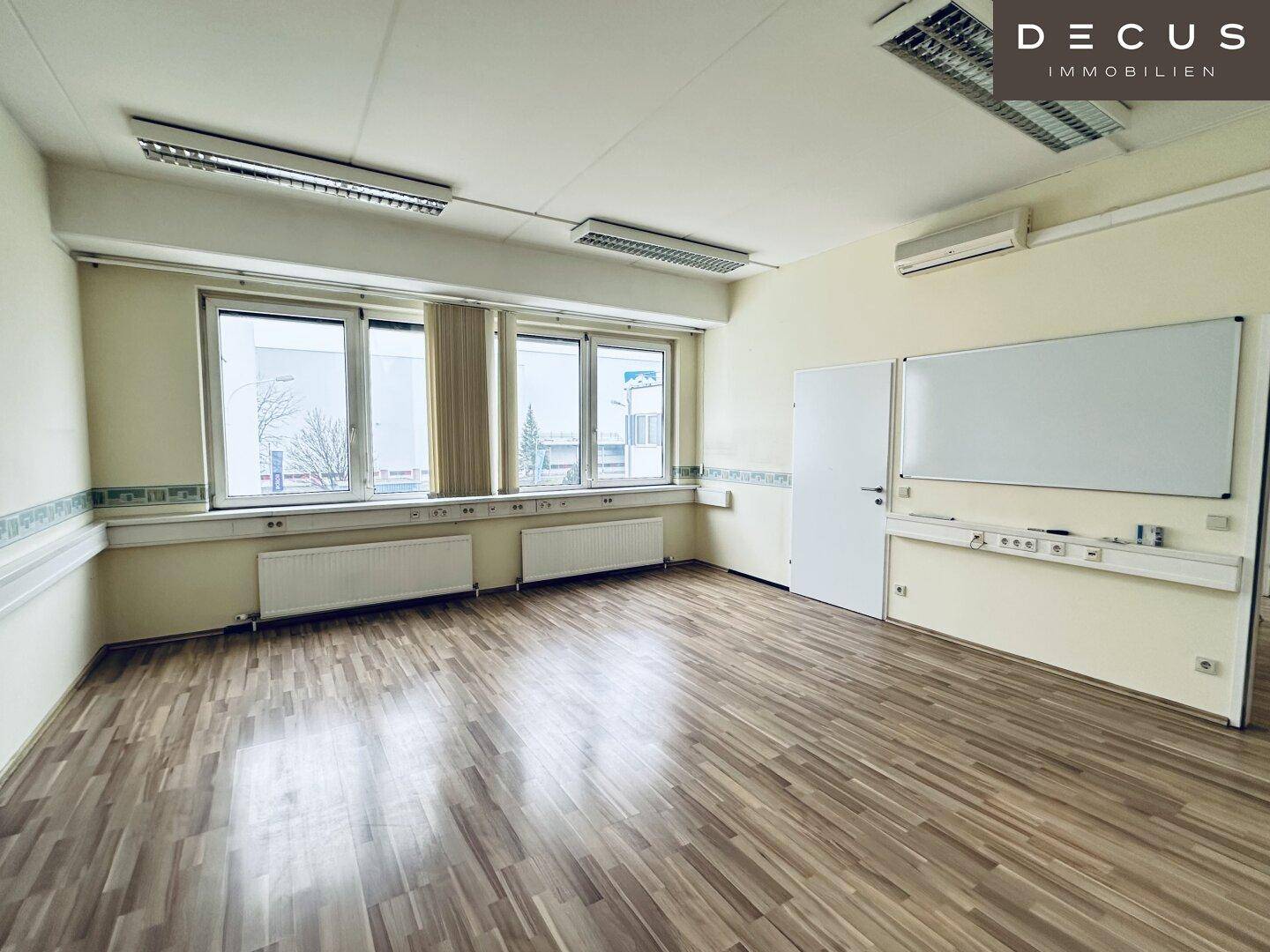 Geräumiges Büro oder Konferenzzimmer mit Laminatboden, breiter Fensterfront und einer Whiteboard-Wand.