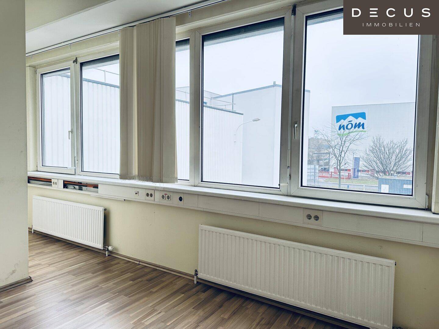Helles Büro mit Laminatboden, breiter Fensterfront und Heizkörpern, bietet Blick auf die Umgebung.