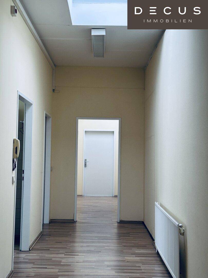 Heller Flur mit Laminatboden, mehreren Türen und einem Oberlicht, das Tageslicht hereinlässt.