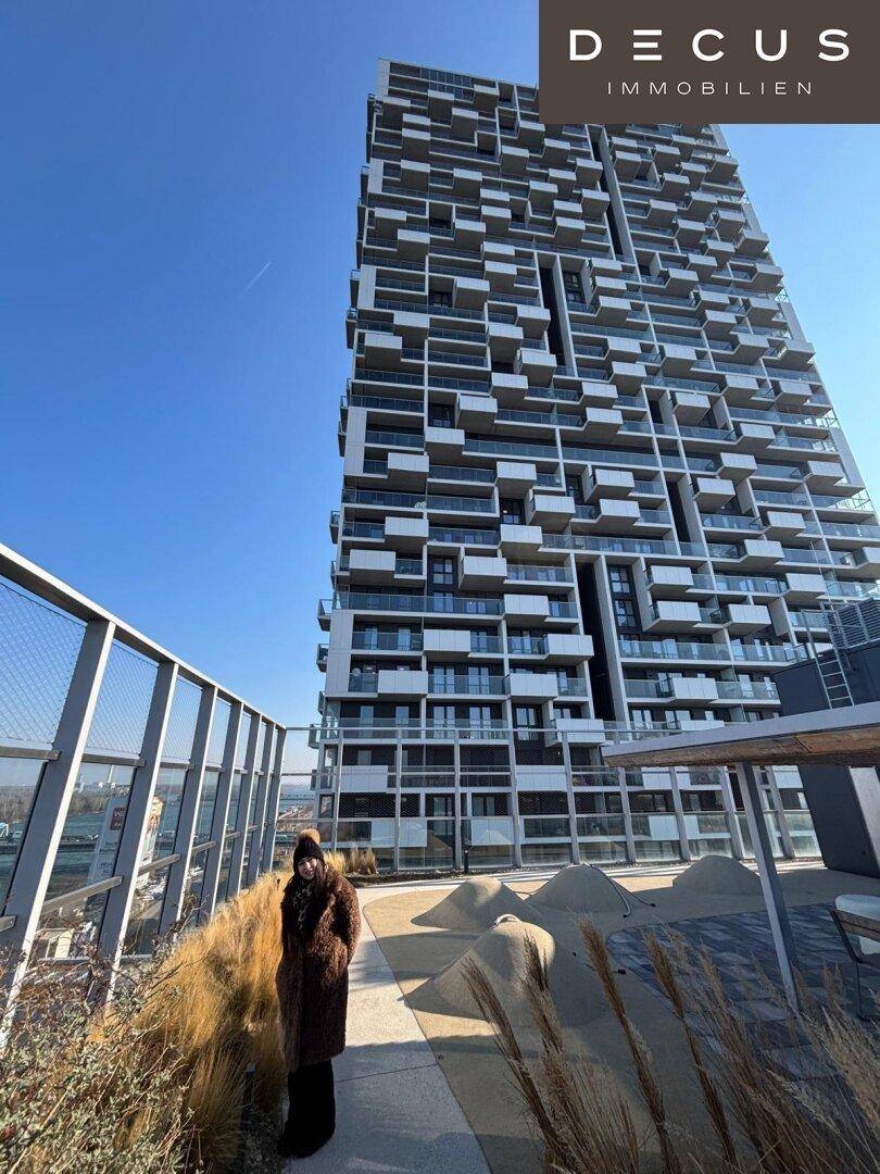 Hohes modernes Gebäude mit vielen Balkonen und einer Person auf der Dachterrasse.